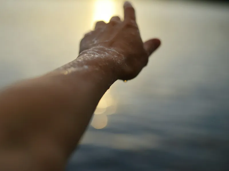 Brazo extendido hacia el agua al atardecer